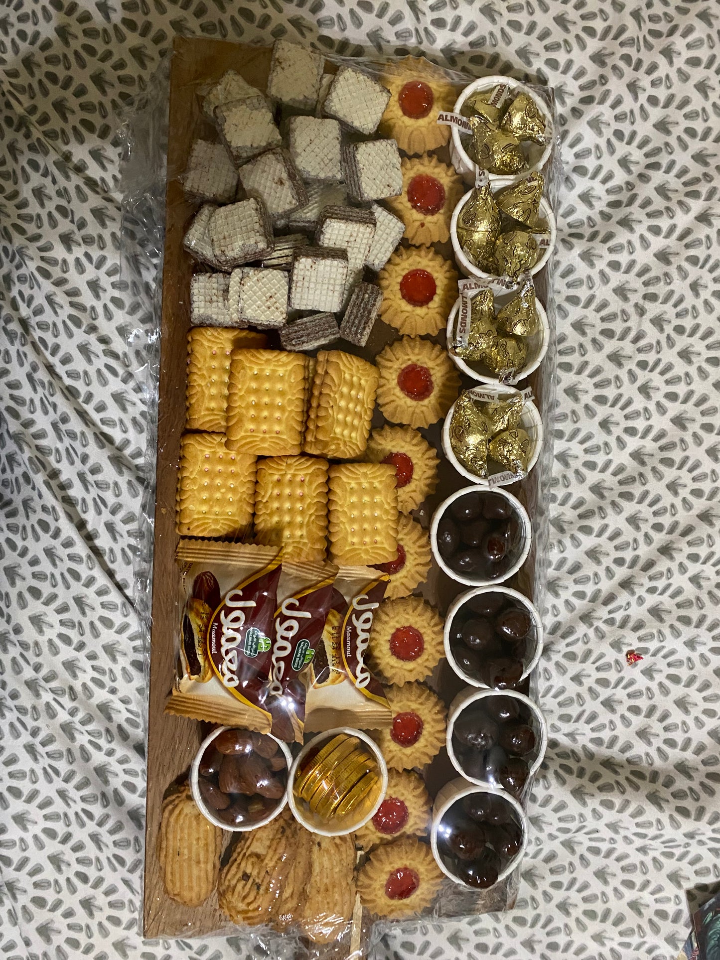Assorted cookies and chocolates on a wooden board with a patterned fabric background